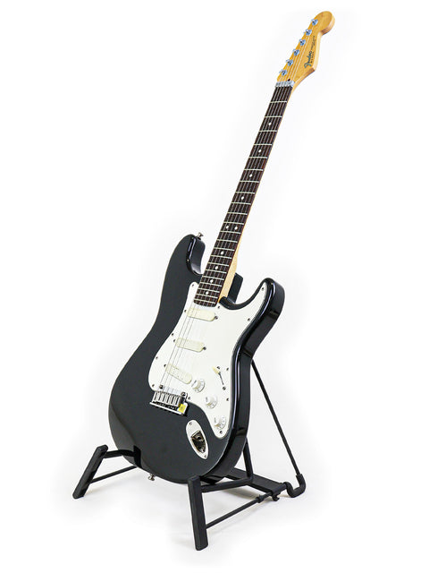 A black guitar, the Fender Strat Plus from 1991, showcased on a stand with a minimalist white background.