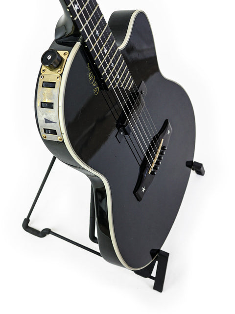 A black guitar, the Gibson Chet Atkins SST from 2001, positioned on a stand for display.