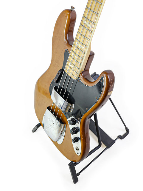 A classic 1974 Fender Jazz Bass guitar displayed on a stand with a white backdrop.
