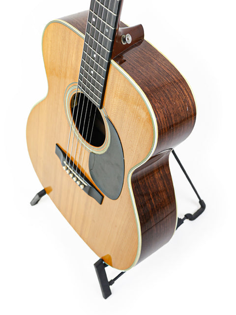 A classic 1976 Vintage Martin 000-28 guitar resting on a stand, contrasted by a simple white background for emphasis.
