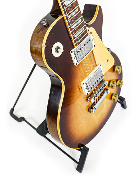 A classic 1979 Gibson Les Paul Standard guitar on a stand, featuring a stark white background for emphasis.