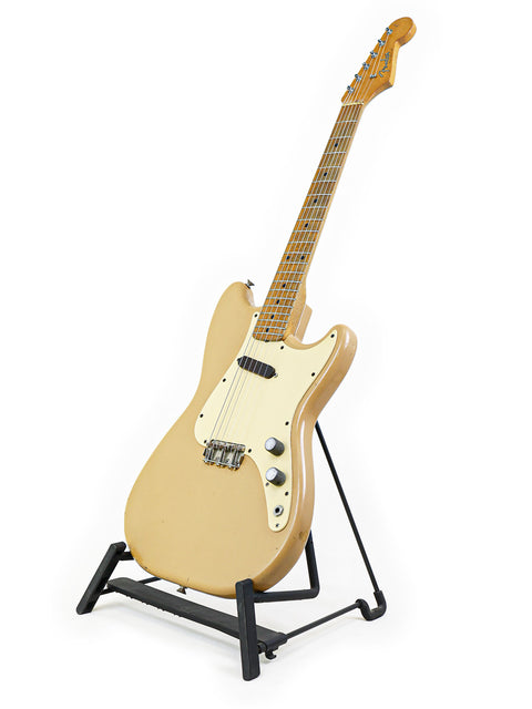 A classic gold Fender Musicmaster guitar from 1957, showcased on a stand with a simple white background.
