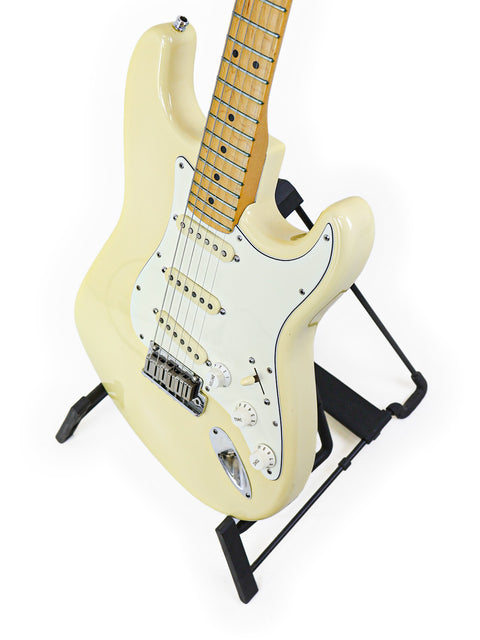 A cream-colored electric guitar on a black stand against a white background.