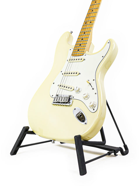 A cream-colored electric guitar on a black stand against a white background.