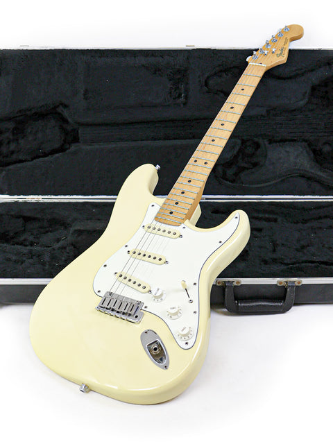 A cream-colored electric guitar with a maple fretboard rests against a guitar case.