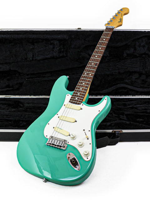 A green Fender Strat Plus Deluxe electric guitar, USA-made in 1989, positioned next to its sturdy case.