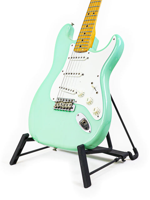 A green electric guitar, the vintage Fender AVRI ‘57 Stratocaster from 1985, displayed elegantly on a stand.