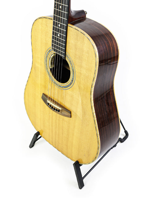 A guitar on a stand against a white background, showcasing its design and craftsmanship, labeled Jim Williams WD-40, Australia 2005.