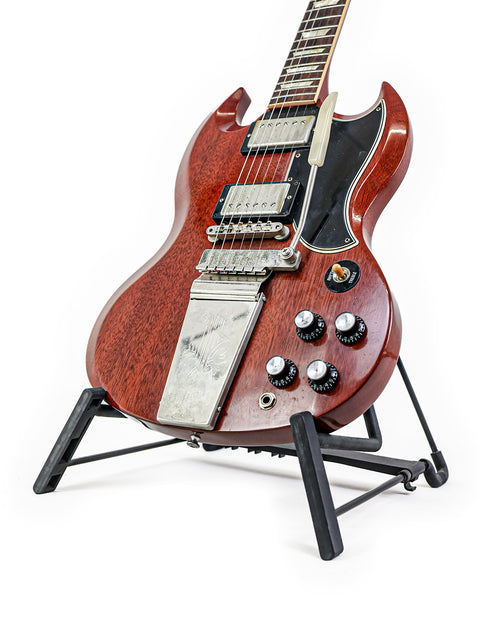 A red Gibson Custom Les Paul SG Standard M VOS electric guitar on a stand, emphasizing its bold color and iconic shape.