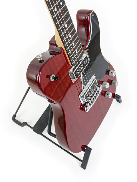 A red electric guitar, Fender Tele-Sonic 2001, displayed on a stand, showcasing its striking black body.