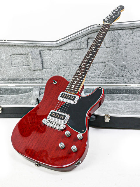 A red electric guitar, the Fender Tele-Sonic from 2001, resting in its case, showcasing its vibrant color.