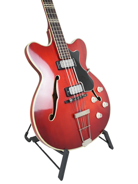 A red electric guitar, the vintage Hofner Verithin Bass from Germany, 1961, elegantly positioned on a stand.