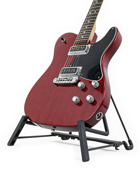 A red guitar, the Fender Tele-Sonic from 2001, elegantly positioned on a stand with a black base, emphasizing its bold design.
