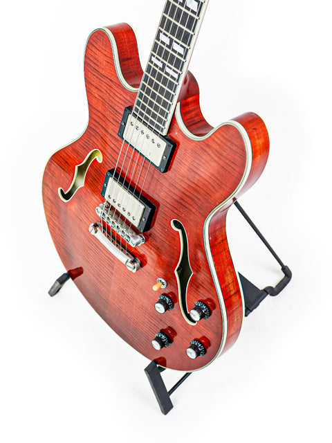 A red semi-hollow electric guitar with F-holes on a white background.