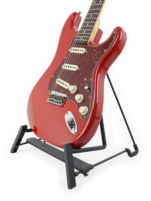 A striking Dakota Red Fender Custom Shop 1961 Stratocaster guitar displayed on a sleek black stand.