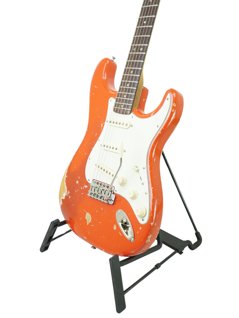 A striking orange Fender Stratocaster from 1979 rests on a stand, highlighted by a bright white background.
