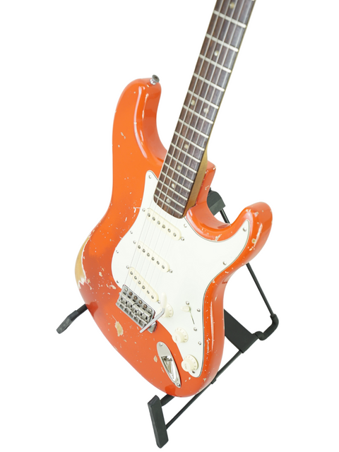 A striking orange guitar, a 1979 Fender Stratocaster, proudly sits on a stand, embodying vintage style and musical history.
