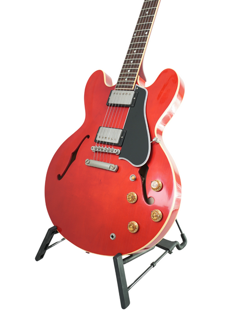 A striking red Gibson Custom ES-335 Aged '59 Reissue guitar with a black body, resting on a stand, showcasing its design.
