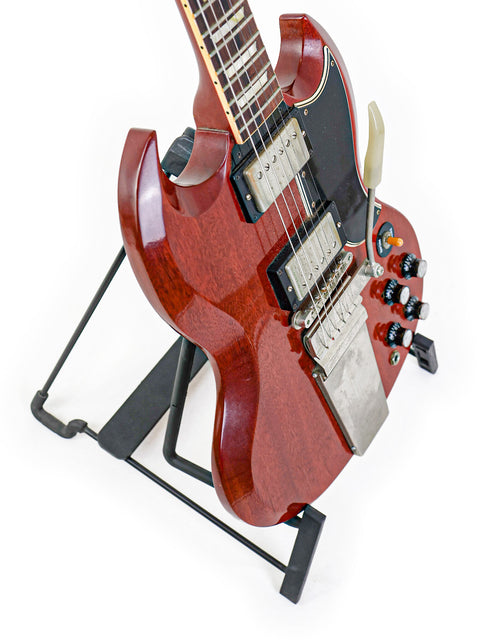 A striking red Gibson Custom Les Paul SG Standard guitar rests on a stand, adorned with a stylish black guitar strap.