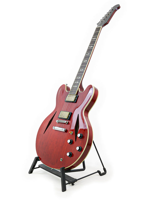 A striking red Gibson Custom Shop Trini Lopez guitar displayed on a stand, set against a bright white backdrop.