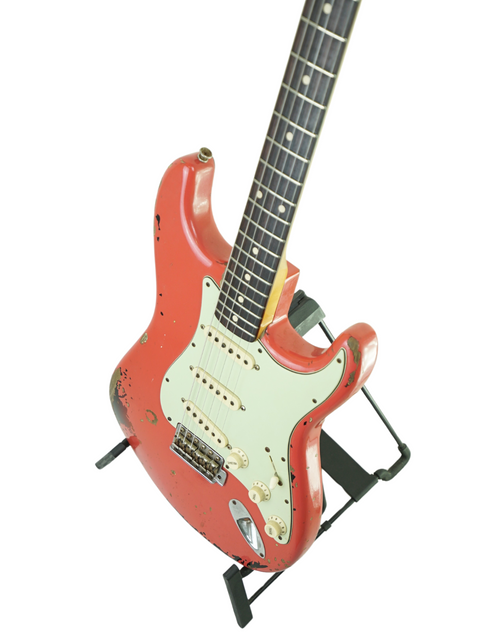 A striking red guitar, the Fender Custom Shop '63 Michael Landau Stratocaster Relic, stands on display against white.
