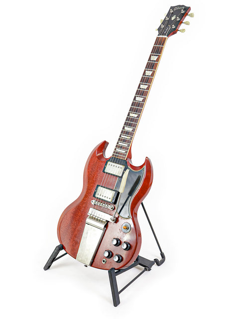 A striking red guitar, the Gibson Custom Les Paul SG Standard M VOS, positioned on a stand with a white background.