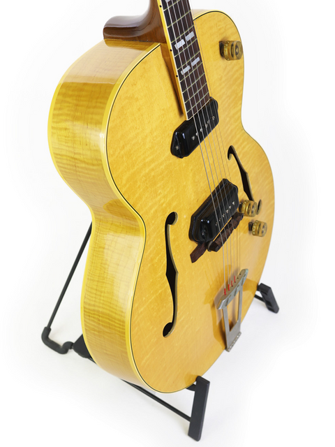 A striking yellow 1952 Gibson ES-300 guitar on a stand, set against a pristine white backdrop, showcasing its vintage charm.
