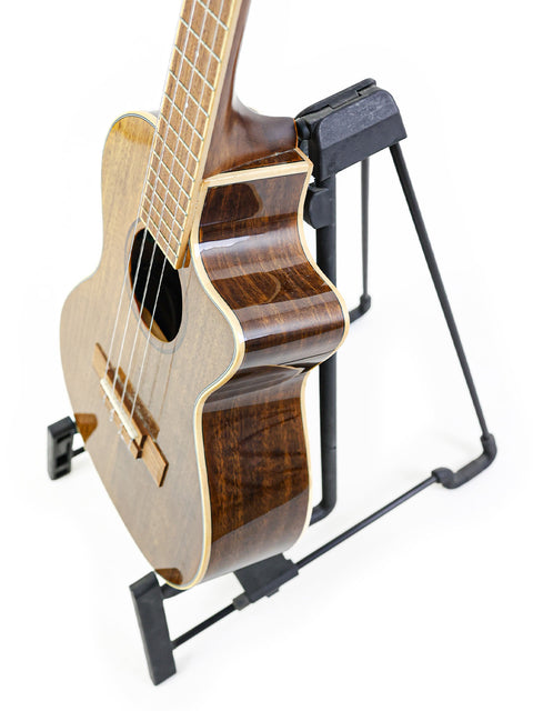 A stunning Kala KA-KTGE-C Hawaiian Koa Tenor Cutaway Ukulele displayed on a stand, highlighting its rich, natural finish.