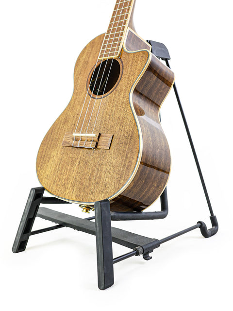 A stunning Kala KA-KTGE-C Hawaiian Koa Tenor Cutaway Ukulele resting on a black stand, highlighting its elegant design.