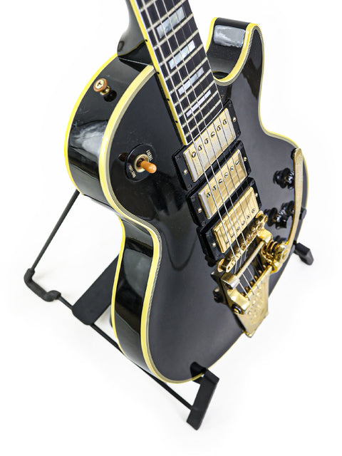 A stunning black and gold Gibson Les Paul Custom B3 guitar from 2004, elegantly positioned on a stand.
