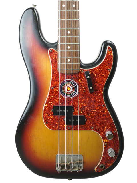 A sunburst electric bass guitar with a round sticker near pickups on a white background.