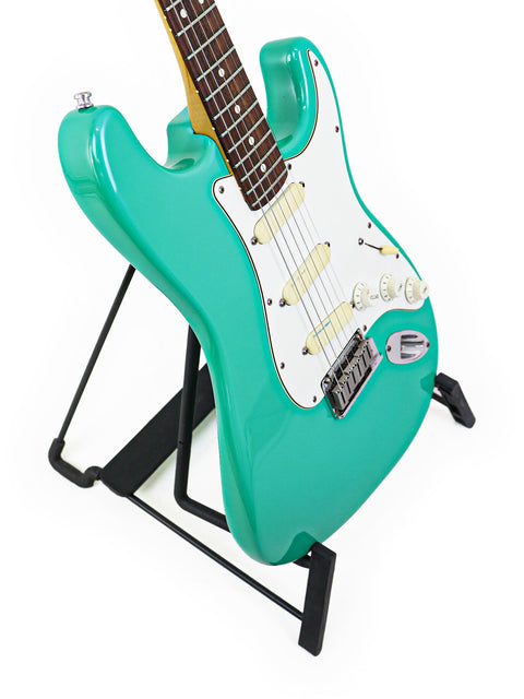 A turquoise electric guitar, the Fender Strat Plus Deluxe from 1989, elegantly positioned on a stand for display.
