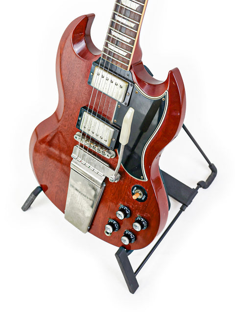 A vibrant red electric guitar, the Gibson Custom Les Paul SG Standard M VOS, elegantly positioned on a stand for display.