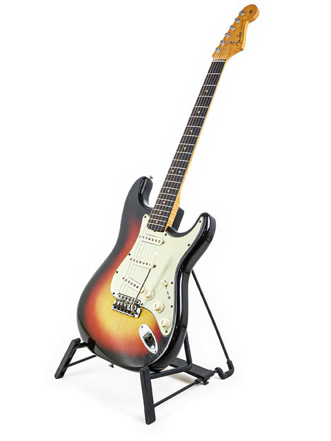 A vintage 1963 Fender L-Series Stratocaster guitar on a stand, showcased with a plain white background.