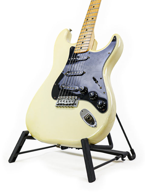 A vintage 1977 Fender Stratocaster guitar in white, beautifully showcased on a contrasting black stand.