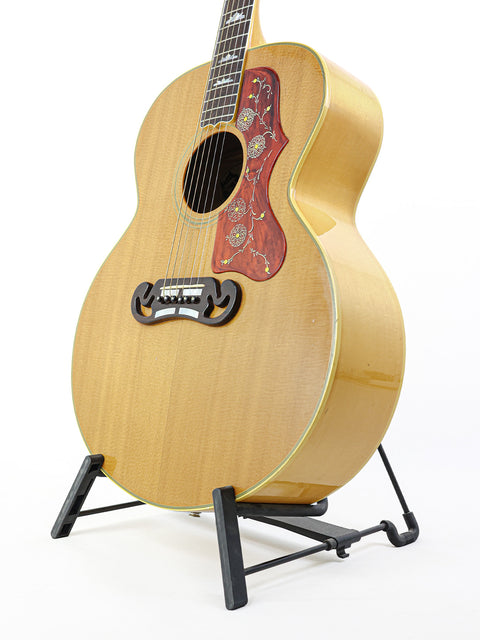 A vintage 1984 Gibson SJ-200 guitar elegantly positioned on a stand, set against a pristine white backdrop.