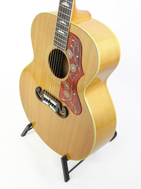 A vintage 1984 Gibson SJ-200 guitar on a stand, prominently featured against a white background.