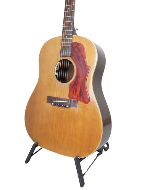 A vintage Gibson J-50 from 1968 stands proudly on a stand, highlighted by a simple white background.
