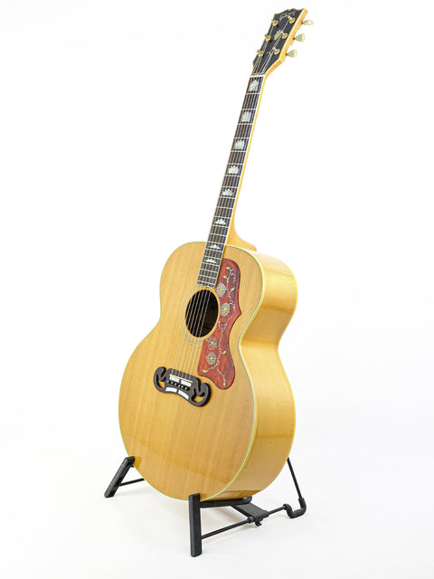 A vintage Gibson SJ-200 guitar from 1984 showcased on a stand against a plain white background.