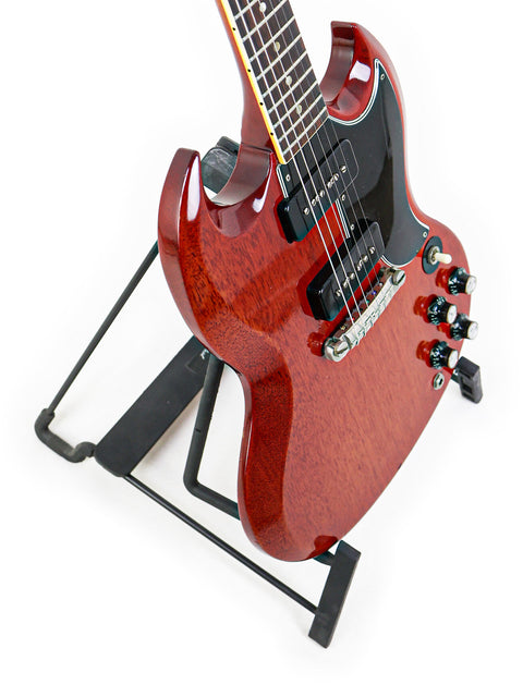 A vintage red Gibson SG Special guitar from 1964/5, elegantly positioned on a stand with a black strap.