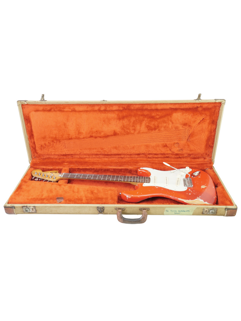 A vintage red guitar, a 1979 Fender Stratocaster, resting in its case on a pristine white surface.