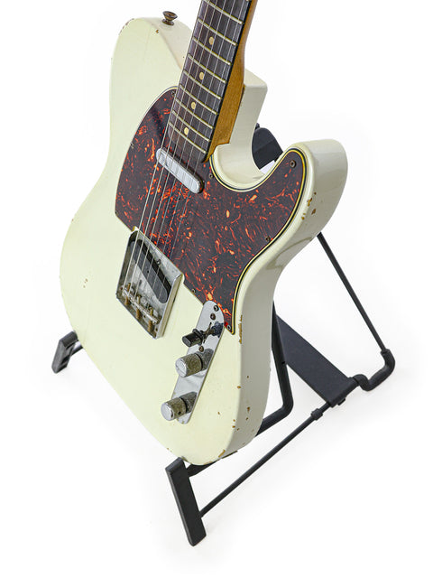 A vintage white Fender Telecaster guitar from 1963, adorned with a black pick guard, resting on a stand.