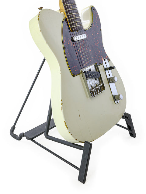 A white 1963 Fender Telecaster guitar on a black stand, highlighting its vintage appeal and craftsmanship.