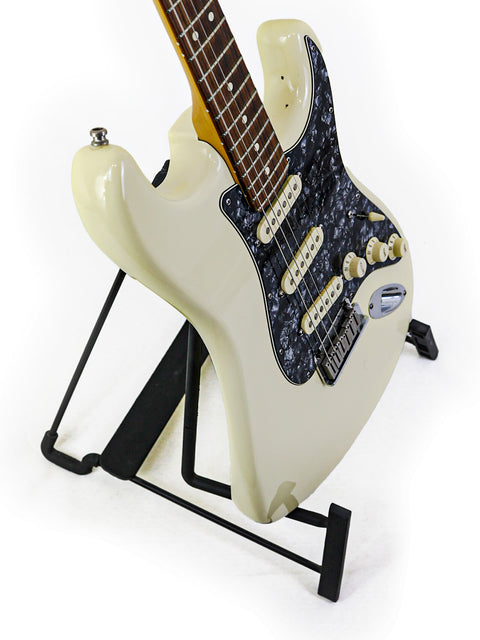 A white guitar, the 2015 Fender Jeff Beck Signature Stratocaster, resting on a black stand, emphasizing its stylish look.