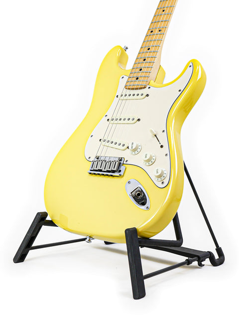 A yellow electric guitar on a black stand against a white background.