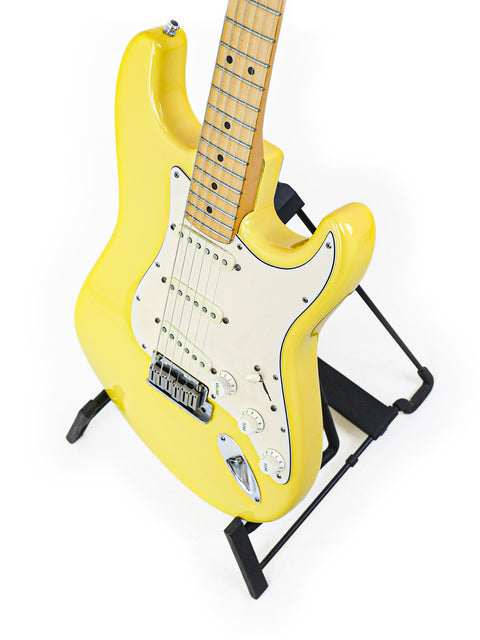 A yellow electric guitar on a stand against a white background.
