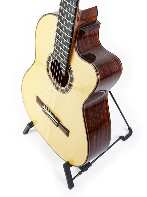 Acoustic guitar on a stand with a light top and dark sides, isolated on white background.