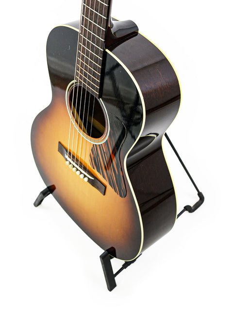 Acoustic guitar on a stand, with a sunburst finish, viewed from a high angle.