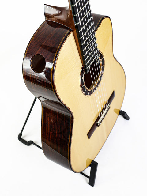 Acoustic guitar on a stand, with a white background.