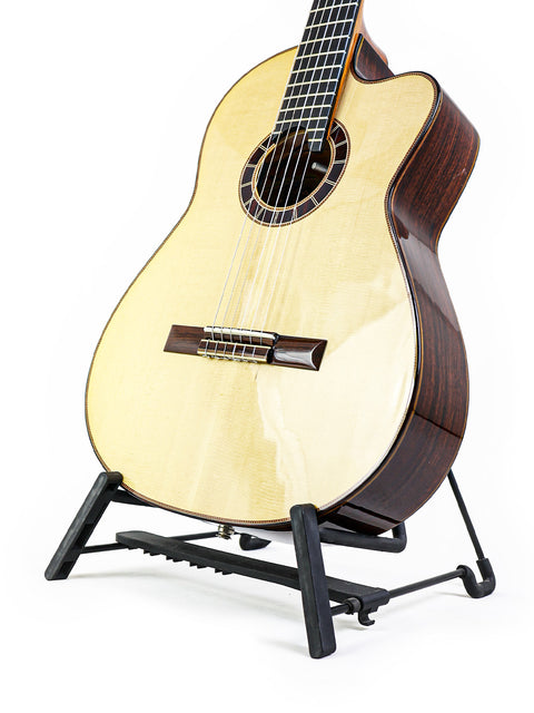 Acoustic guitar on black stand against white background.